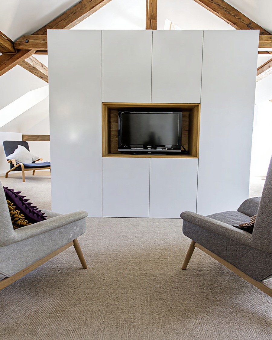 Attic conversion sitting room, mid-century chairs, built-in TV cabinet with timber inset, exposed roof trusses