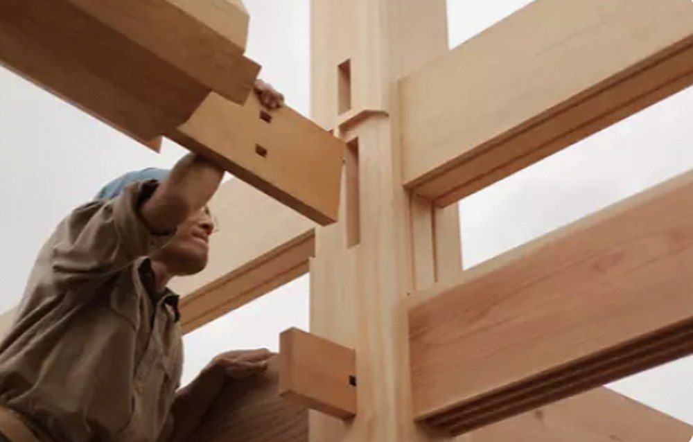Master carpenter inspecting a hand-cut Japanese-style heavy timber post and beam joint