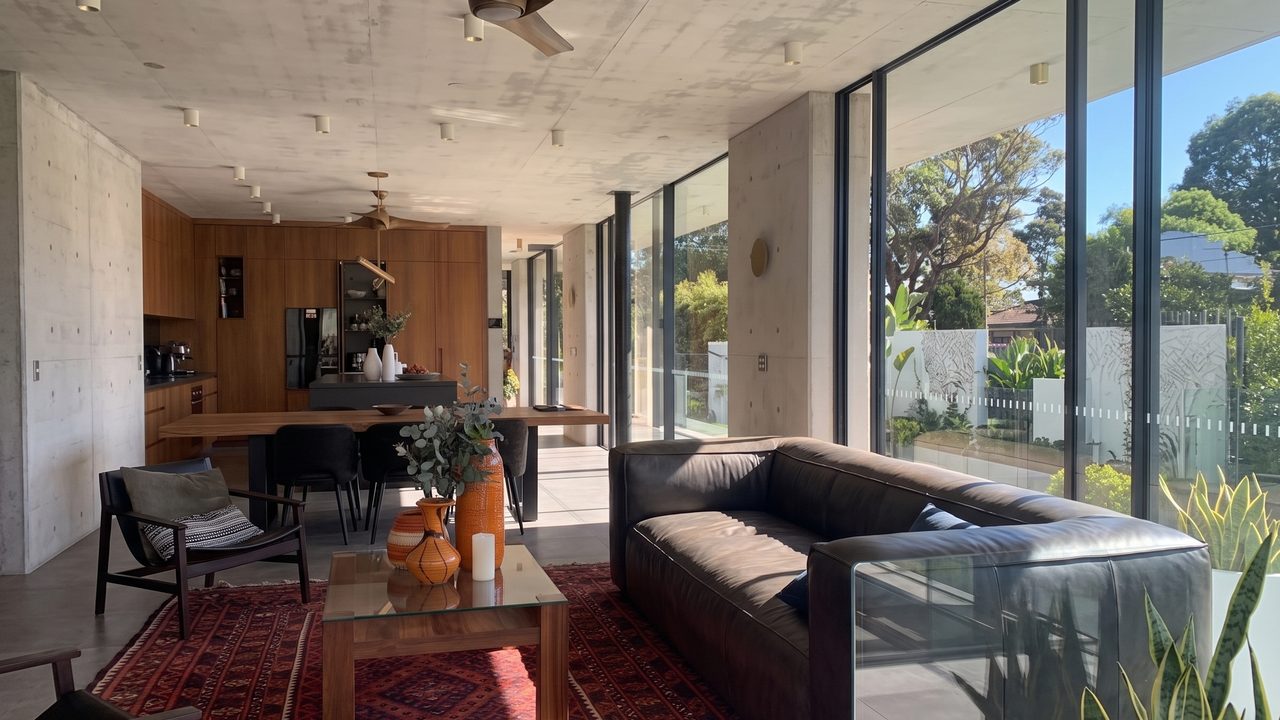 Open-plan living and dining room with concrete ceiling, leather sofa and floor-to-ceiling glazing to the garden