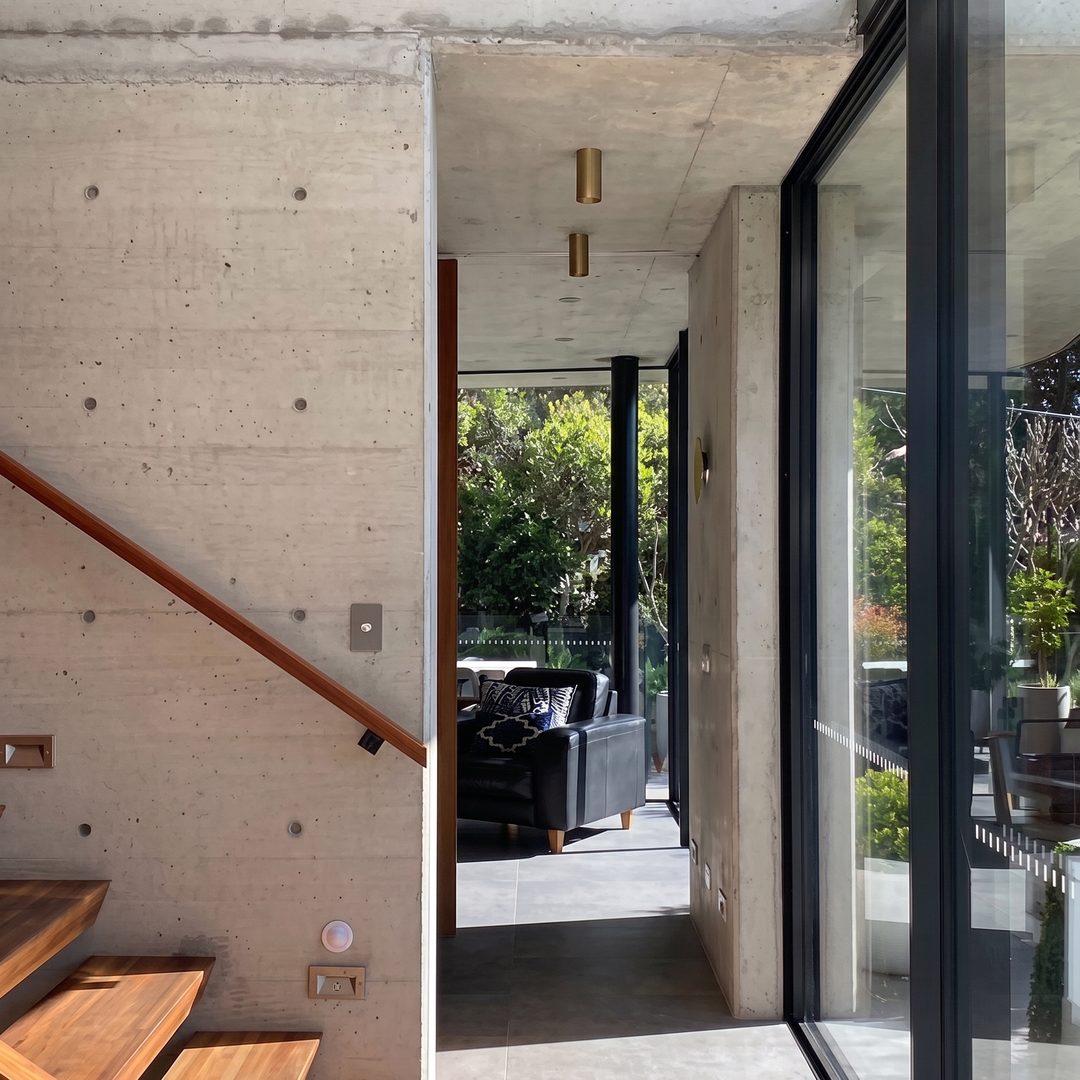 Board-formed concrete stairwell with floating timber treads and full-height glazing