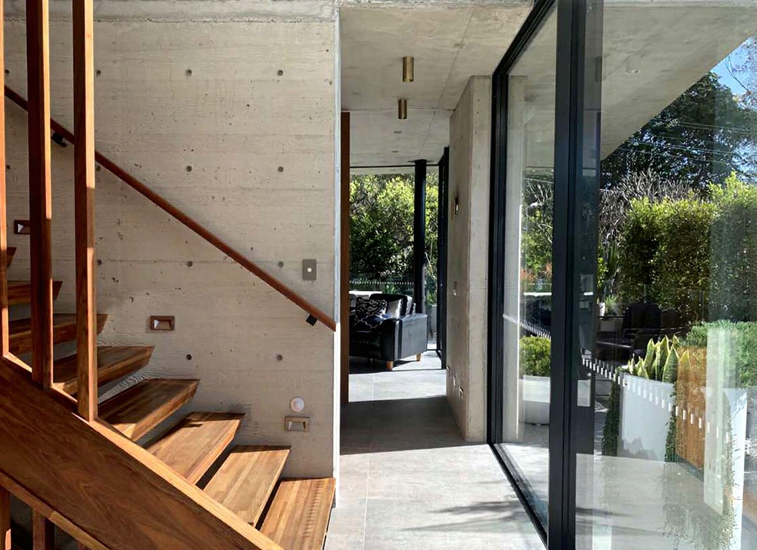Open timber-and-steel staircase against board-formed concrete with sliding glass to a courtyard, precision engineering, built to last.